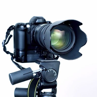 Digitale Kamera mit Objektiv auf einem Stativ, Hintergrund in Weiß.